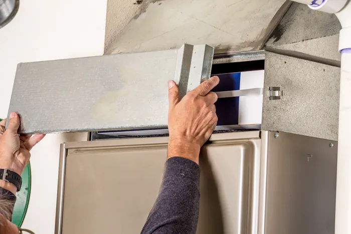 A technician lifting a furnace access door clear of the filter slot
