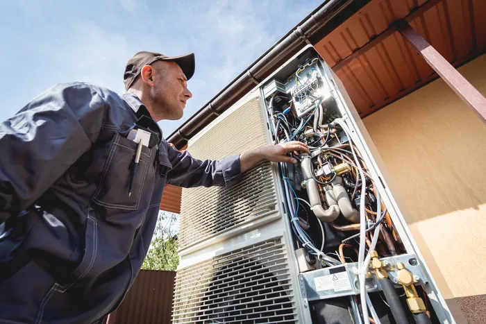 An HVAC technician with an outdoor unit's cover removed, working on the compressor bay