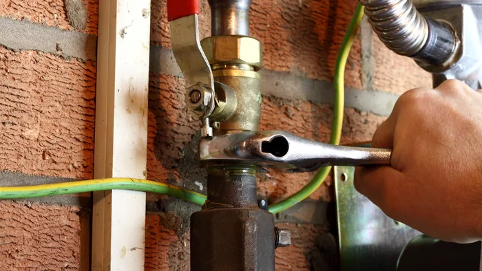A certified gas fitter tightening a brass shut-off valve on a home gas line